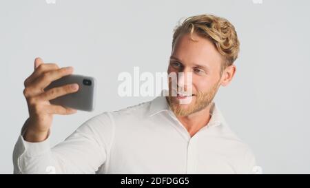 Handsome smiling bearded man in shirt having video call discussing new business project using smartphone over white background. Modern technology Stock Photo