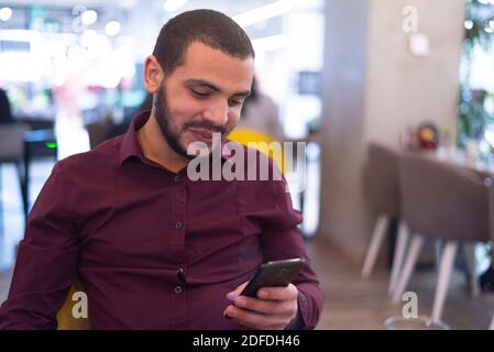 Young frican man chatting, writing message smart phone inside modern restaurant Stock Photo