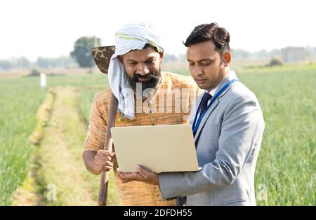 Farmer with businessman using laptop on agriculture field Stock Photo