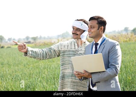 Farmer with businessman using laptop on agriculture field Stock Photo