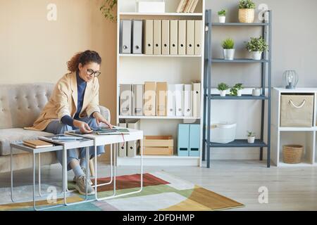 Female designer in eyeglasses sitting at the table and working with pictures at office Stock Photo