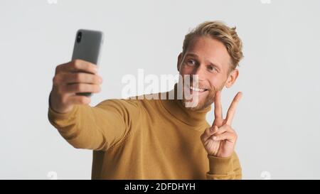 Attractive stylish bearded man showing peace gesture making selfie isolated on white background Stock Photo