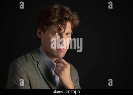 Handsome young freelancer man looking at camera with a strong look wearing suit jacket isolated on black background. Copy space on the right Stock Photo