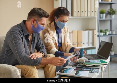 Two designers in protective masks working with professional photos in team during their meeting at office Stock Photo