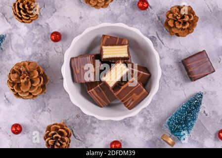German layered winter cake pralines called 'Baumkuchen' glazed with chocolate in bowl, surrounded by seasonal Christmas decoration Stock Photo