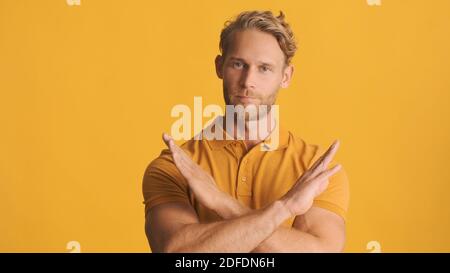 Handsome serious bearded man confidently showing crossed hands on camera over colorful background. No expression Stock Photo