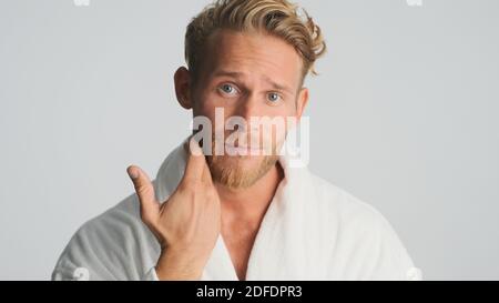 Attractive bearded man in bathrobe thinking to shaved posing on camera over white background Stock Photo