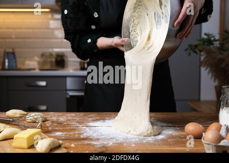 Young beautiful woman kneading dough at a wooden table in kitchen. Housewife hobbies concept. Stock Photo
