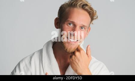 Attractive bearded man in bathrobe joyfully posing on camera over white background Stock Photo