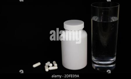 Glass with water. White medical bottle and pills on a black background. Stock Photo