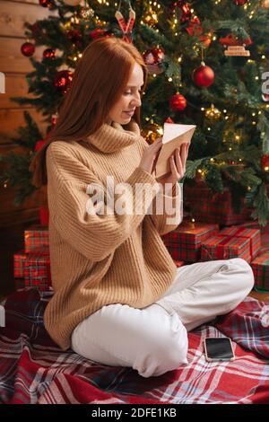 Attractive young woman getting Christmas greeting card from her beloved on background of xmas tree. Stock Photo