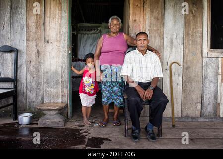 Disabled person paralyzed from Decompression sickness (DCS) due to intense lobster fishing using scuba diving methods, sitting with his mother and grandson outside his wooden shack. Brus Laguna, Mosquitia, Honduras Stock Photo