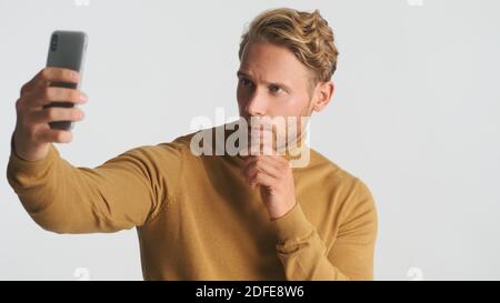 Handsome stylish bearded man taking selfie on smartphone over white background. Male model posing in studio Stock Photo