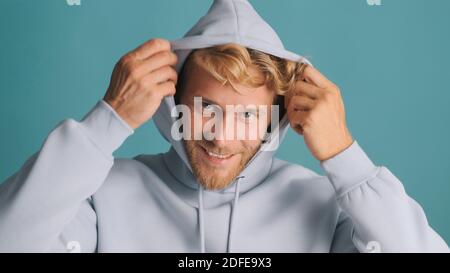 Handsome stylish bearded guy in hood looking happy over colorful background. Attractive casual male model posing in studio Stock Photo