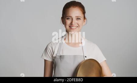 Attractive friendly waitress in apron with tray happily looking in camera isolated Stock Photo