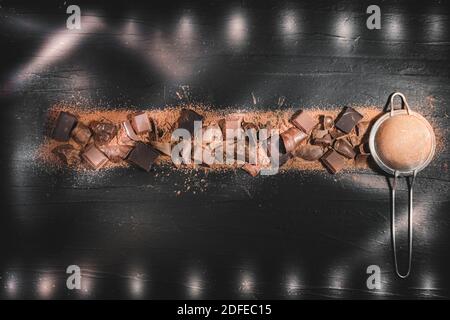 Pieces of different types of chocolate, mix of dark and milk chocolate scattered over sprinkled cocoa powder top view. Stock Photo