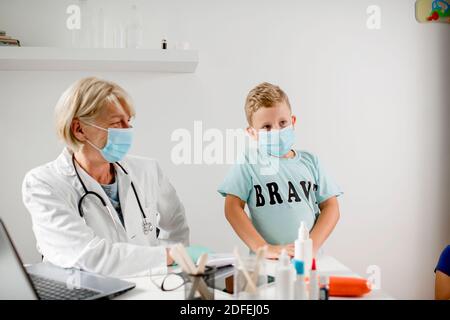 Smiling doctor talking with a boy. They are wearing a protective face mask. Stock Photo