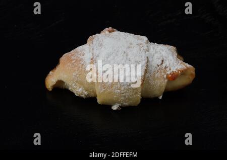 Homemade jam bun sprinkled with powdered sugar close-up on a dark wooden surface. Selective focus. Stock Photo
