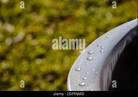 Close-up of water droplets on smooth metal surface against blurred green background. Stock Photo