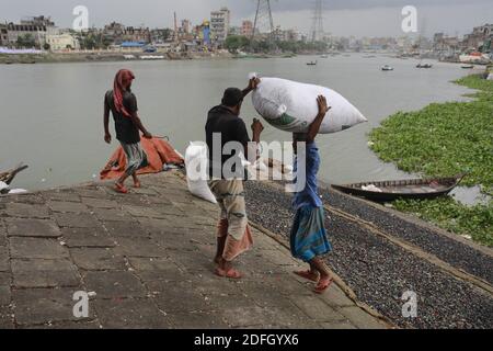 Bangladeshi workers collect pieces of wastage plastic materials after dry them under the sun on the bank of Burigonga River, in Dhaka, Bangladesh, on September 26, 2020. Around 12-13 years ago, the Buriganga River was a popular waterway for communication and transporting goods as it flowed through Rasulpur in Kamrangirchar. However, the Burigang can hardly be called a river anymore as it has shrunk so much that it is now narrower than a canal. Locals now call it a 'plastic river', even though they admitted to polluting it with plastic waste. In Dhaka city, more than 14 million pieces of poly b Stock Photo