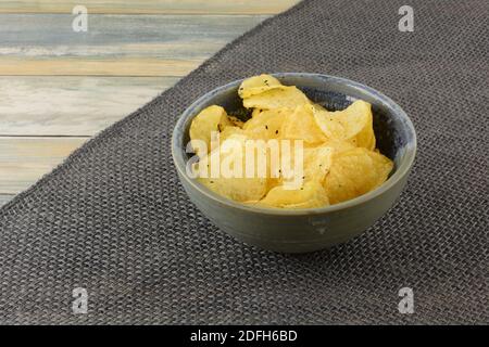 Italian black truffle potato chips in ceramic snack bowl on burlap table runner on table Stock Photo
