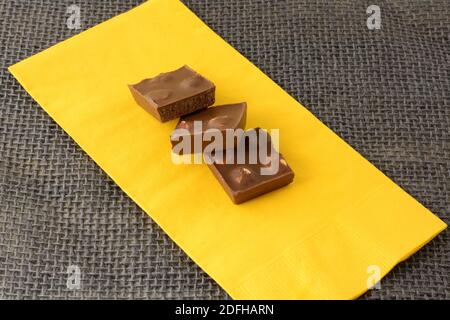 Three hazelnut milk chocolate bar pieces on yellow napkin on burlap Stock Photo