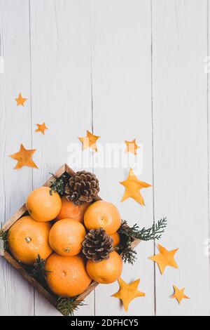 Winter minimalistic still life. Tangerines and cones in a wooden box on a light wooden table. Stock Photo