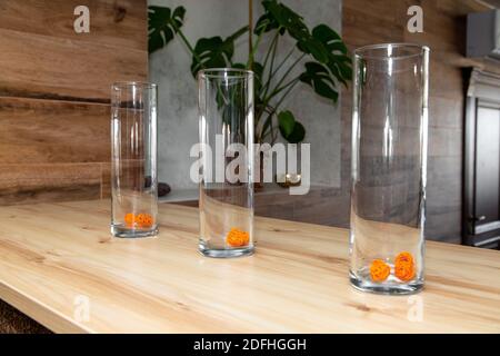Three decorated glasses stand in a row on a natural wood table top. In the background is a Monstera flower. Stock Photo