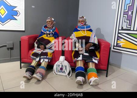 Johannesburg, South Africa. 19th Nov, 2020. Traditionally dressed, South African artist Esther Mahlangu (l) and a relative are sitting in a gallery where Mahlangu's works are exhibited. The 85-year-old artist belongs to the Ndebele tribe, which is mainly at home in the north of South Africa. (To dpa From tradition to world fame: South African artist Esther Mahlangu) Credit: Kate Bartlett/dpa/Alamy Live News Stock Photo