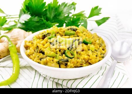 Indian national dish kichari made of mung bean, rice, stalk celery, spinach, hot pepper and spices in a bowl on a napkin, ginger on light wooden board Stock Photo