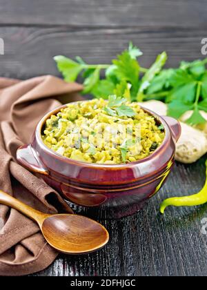 Indian national dish kichari made of mung bean, rice, celery, spinach, hot pepper and spices in a bowl on a towel, ginger and spoon on black wooden bo Stock Photo