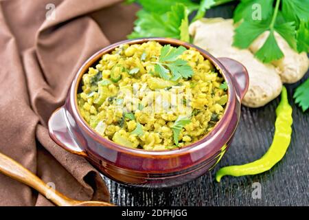 Indian national dish kichari made of mung bean, rice, celery, spinach, hot pepper and spices in a bowl on a towel, ginger and spoon on wooden board ba Stock Photo