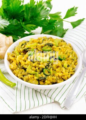 Indian national dish kichari made of mung bean, rice, stalk celery, spinach, hot pepper and spices in a bowl on a striped napkin, ginger on wooden boa Stock Photo