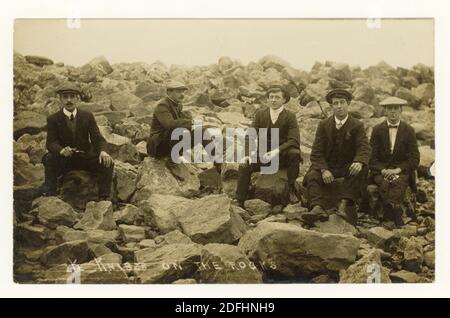 Early 1900's postcard of young men in flat caps and wearing their 'Sunday best' clothes sitting on rocks - His Knibs written on front - circa early 1920's,  U.K. Stock Photo