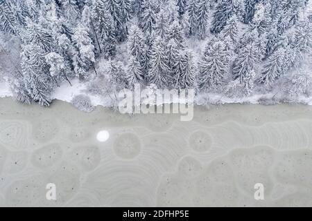 An aerial drone looking down captures patterns, shapes, holes and cracks in frozen lake ice. Stock Photo