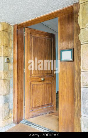 Half opened front wooden door and door sign at yellow and gray decorative uneven stone bricks wall Stock Photo