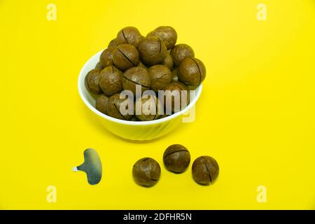 Macadam nuts in a white cup isolated on yellow background.  Stock Photo