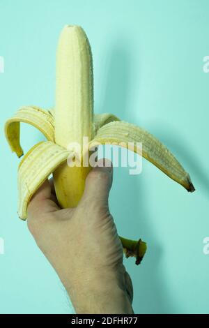 A half-peeled banana in a human hand. Isolated not blue background. Stock Photo