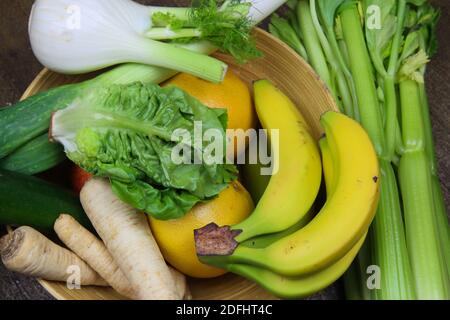 View on bowl with healthy fresh raw winter food: celery sticks, bananas, fennel and parsley roots, salad, grapefruits Stock Photo