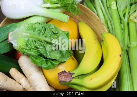 View on bowl with healthy fresh raw winter food: celery sticks, bananas, fennel and parsley roots, salad, grapefruits Stock Photo