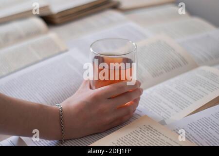 A hand with a silver bracelet holding a cup of tea with a double bottom on books pages - horizontal photo Stock Photo