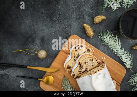 Christmas composition with stollen cake on a wooden board, coffee cup and cutlery on dark background. Flat lay, top view Stock Photo