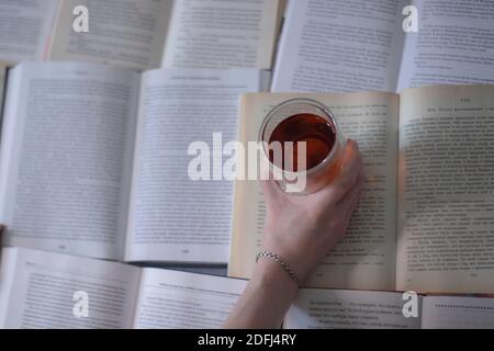 A hand with a silver bracelet holding a cup of tea with a double bottom on books pages - horizontal photo Stock Photo