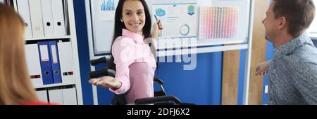 Young woman in wheelchair teaches group of business people at blackboard in office Stock Photo