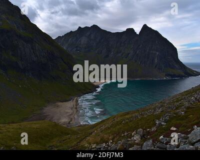 Stunning view of Kvalvika Beach with wild surf surrounded by steep rugged mountains and rocky meadows on cloudy day in late summer in Norway. Stock Photo