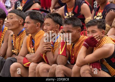 Young Naga tribesmen wearing  traditional attire  siting in central arena of Kisama Village in Nagaland India on 4 December 2016 Stock Photo