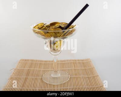 A cocktail glass filled with gold coins on a doormat. Concept about the world of party and money. Stock Photo