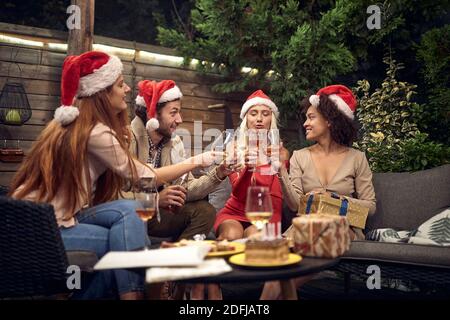 drunk young adults celebrating with santa clause hats, toasting, drinking wine Stock Photo