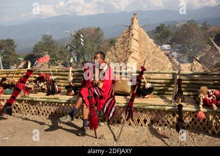 An old naga warrior dressed in traditional attire siting with traditional  weapons kept by his side in village kisama Nagaland India 2 December 2016 Stock Photo