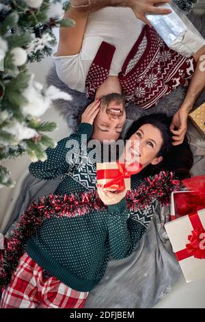 top view of happy young, beautiful,  Caucasian couple laying on the floor at christmas morning, cuddling each other, smiling, enjoying, with wrapped p Stock Photo